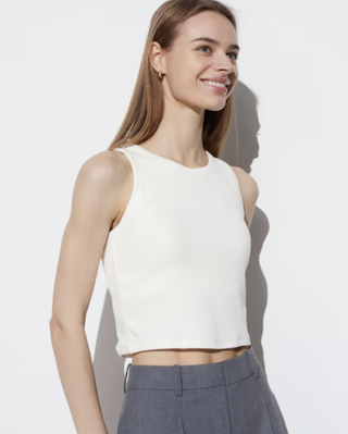 a model wearing a cropped tank top and high waist trousers while standing in front of a plain wall