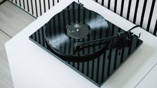 An angled overhead view of the Pro-Ject E1.2 turntable in black on a white piece of furniture