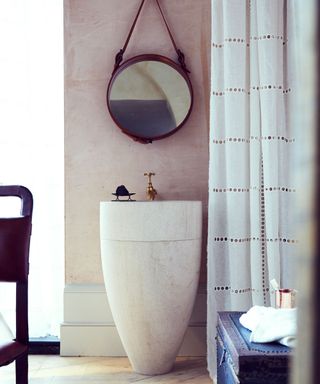 freestanding stone basin with round leather framed mirror and sheer white curtain
