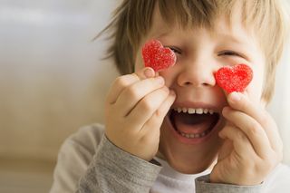 A little boy holds two heart-shaped sweets up to his face and smiles broadly