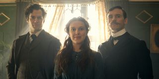 Enola Holmes Henry Cavill Millie Bobbie Brown and Sam Claflin stand together in front of a window