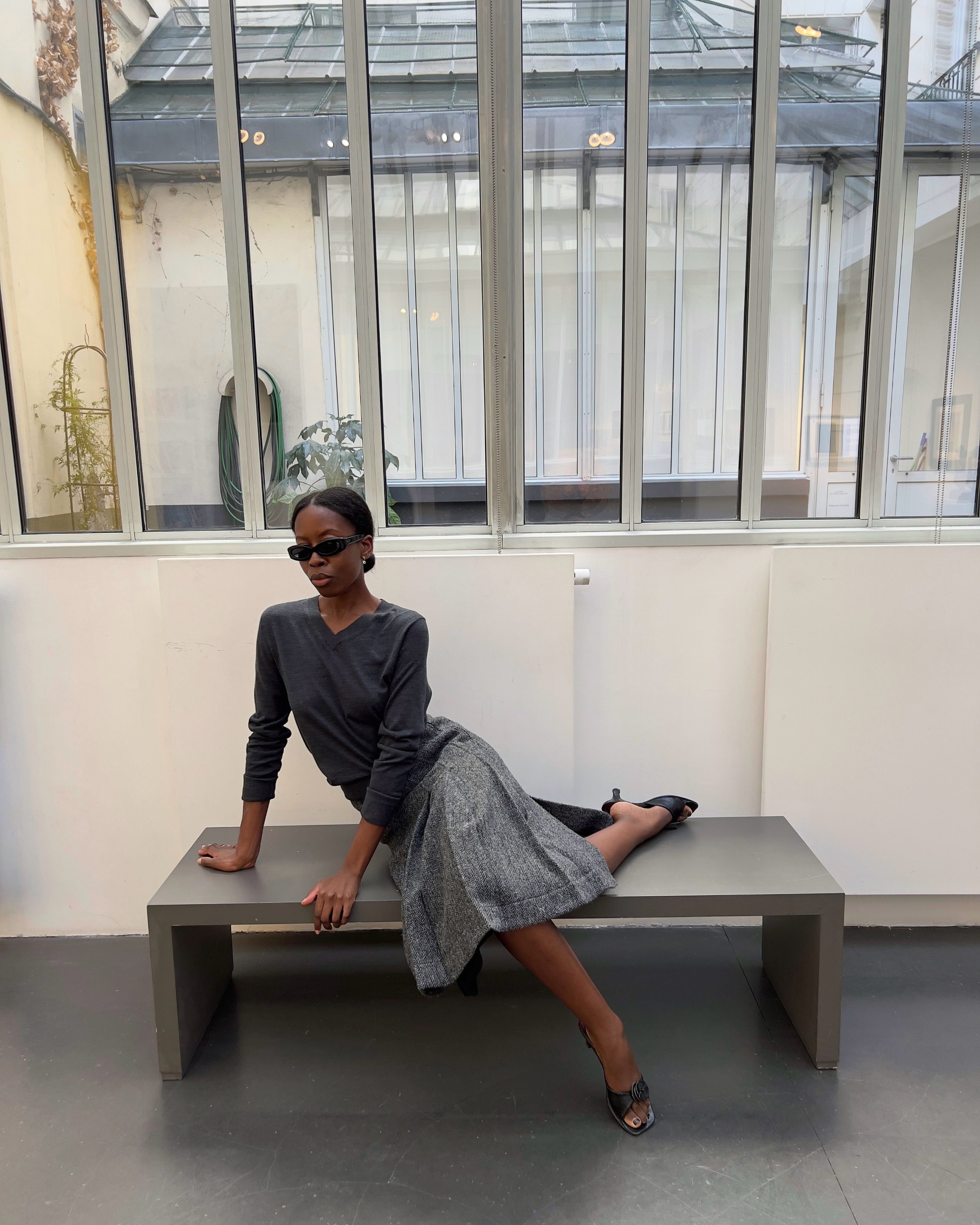 Sylvie Mus wearing a high v-neck sweater, pleated skirt, and kitten-heel sandals.