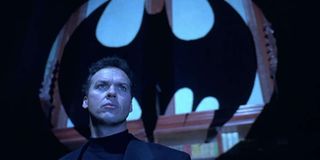 Batman Michael Keaton stands in front of the Bat Signal