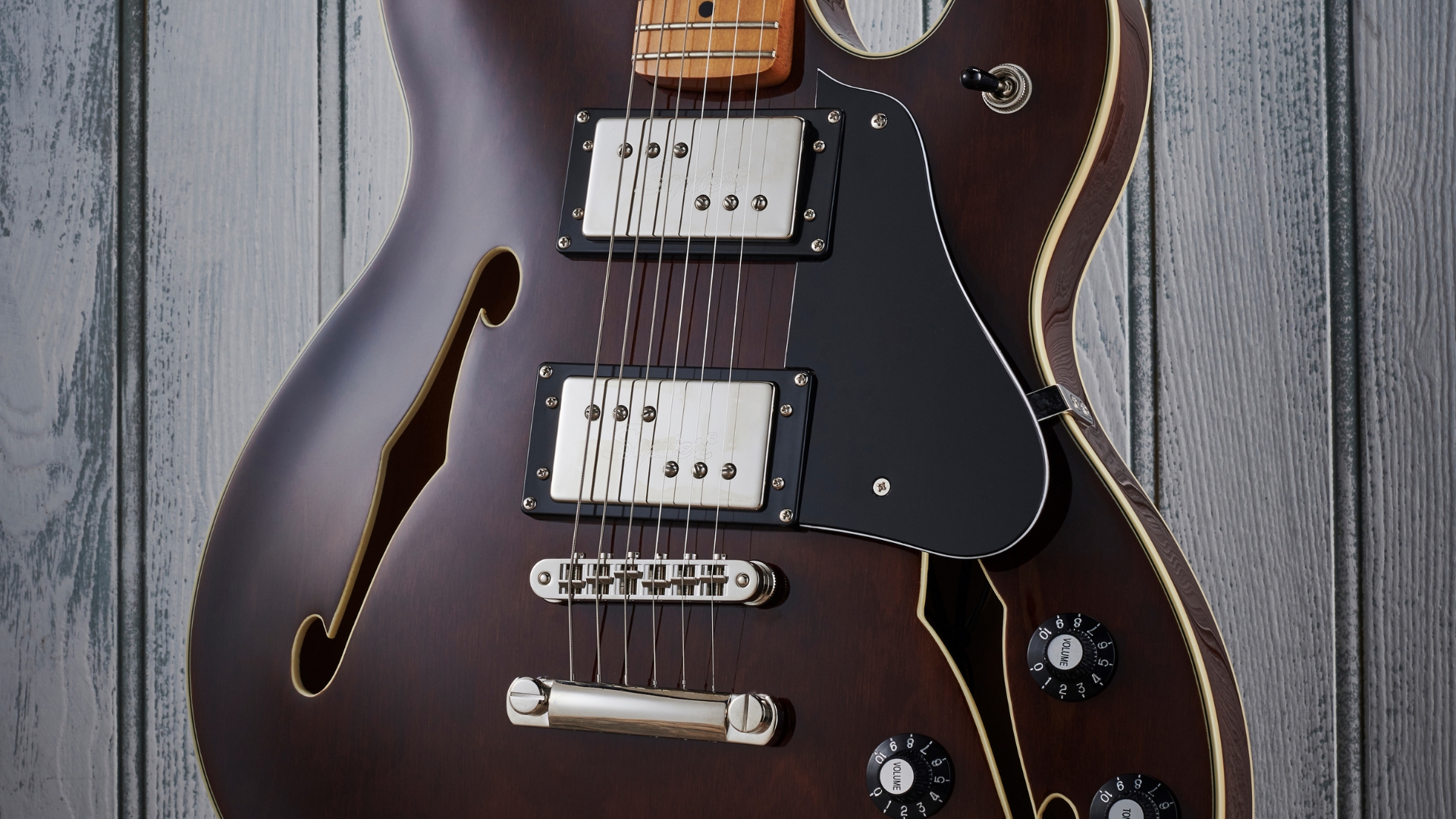 A Squier Classic Vibe Starcaster electric guitar leaning against a wooden wall