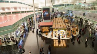 A shot of the retail section of Barcelona-El Prat Airport from above, with passengers walking around with 