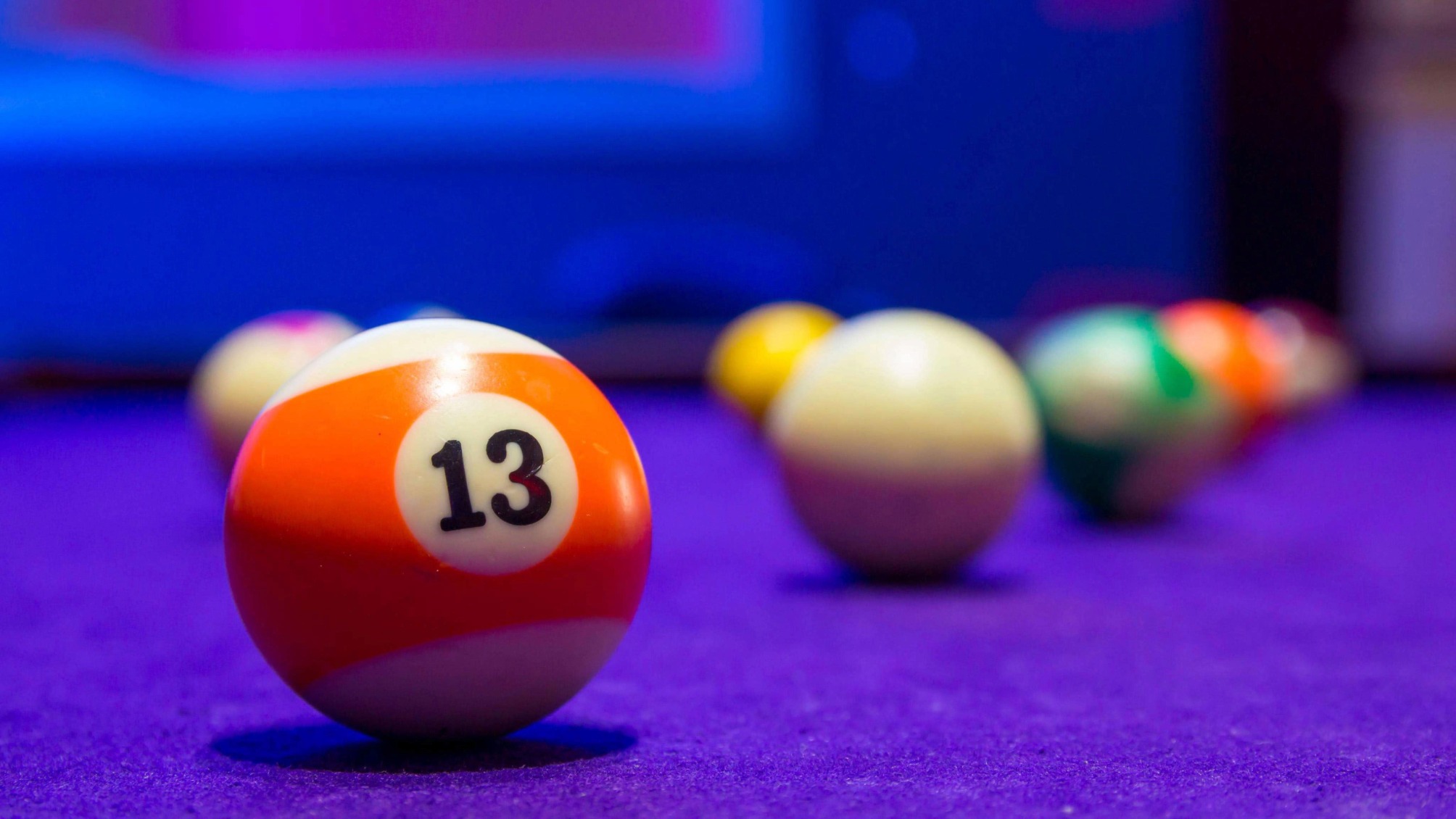 Billiard balls in a pool table. focus on the orange number 13 ball.