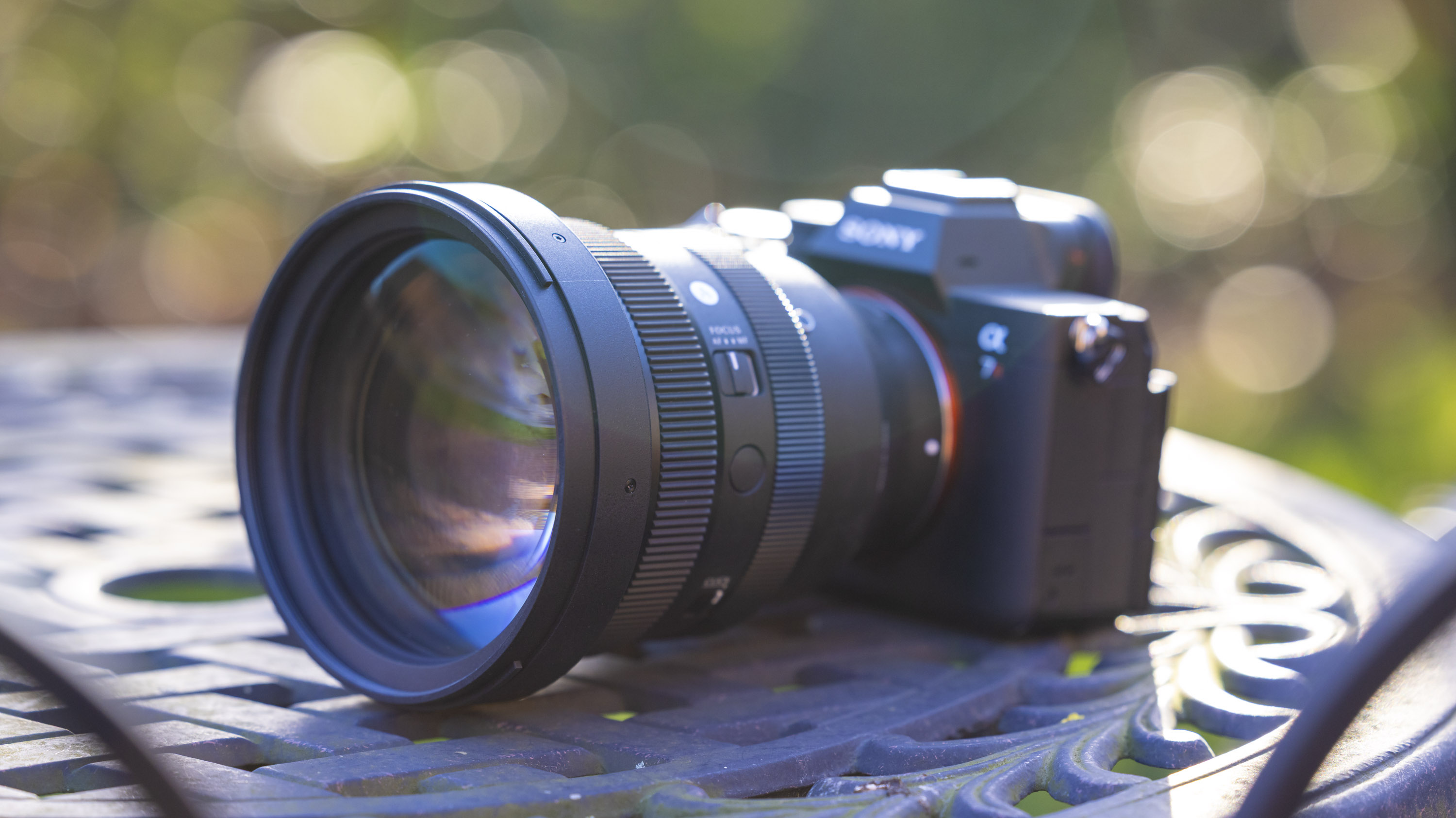 Sigma 135mm f1.4 DG Art lens attached to a Sony A7R IV body positioned on a metal garden table outdoors with lots of bokeh in the background