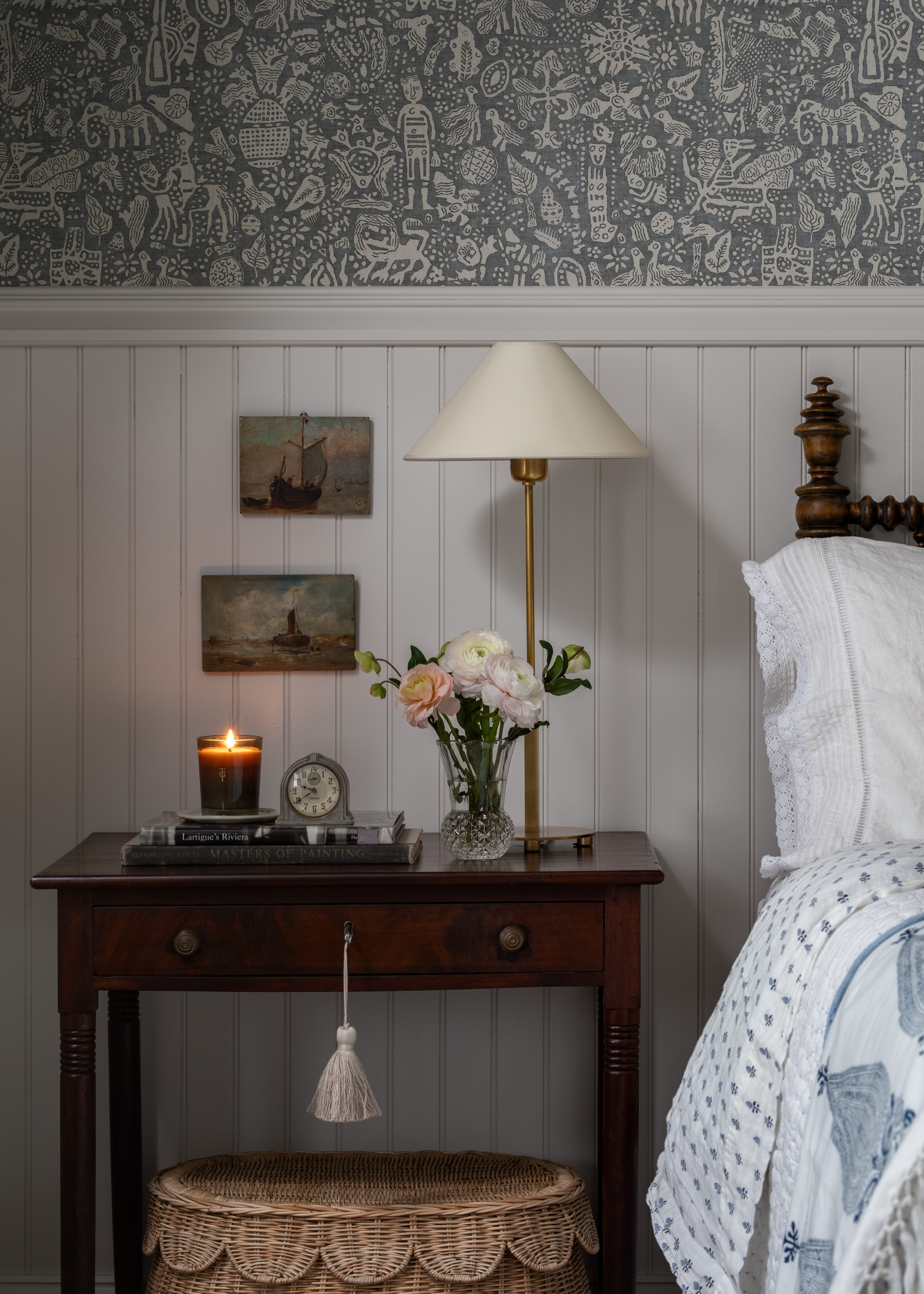 dimly lit bedroom featuring a walnut wood nightstand holding assorted objects and a scalloped rattan dresser underneath
