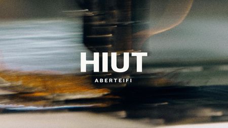 A blurred, dynamic close-up background features a sewing machine needle in motion, with the bold white text "HIUT ABERTEIFI" superimposed in the center.
