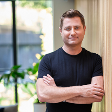 Headshot of George Clarke. He is smiling with his arms folded