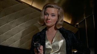 Honor Blackman smiles while she holds a gun in Goldfinger.