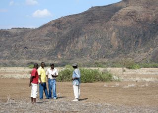 A Kenyan survey team explores for drill sites in the rift valley in 2009. Below the flat plain under their feet are more than 150 meters of ancient lake deposits discovered by the team's drilling project. A wall of upfaulted lavas rises steeply behind them.