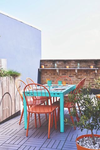 Spillett house: outdoor roof terrace with grey decking, blue table and red dining chairs