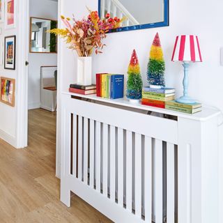 White painted wall with gallery wall, radiator covered with mantelpiece and decorated