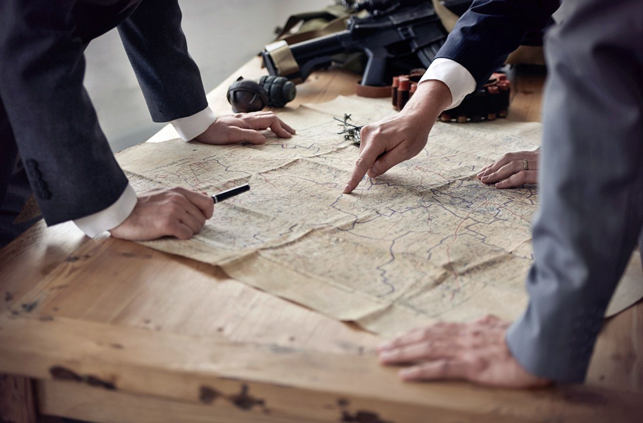 Three men in suits discussing plans while looking at a map lying on a table