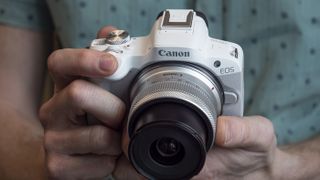 Canon EOS R50 in the hand focused on 18-45mm lens