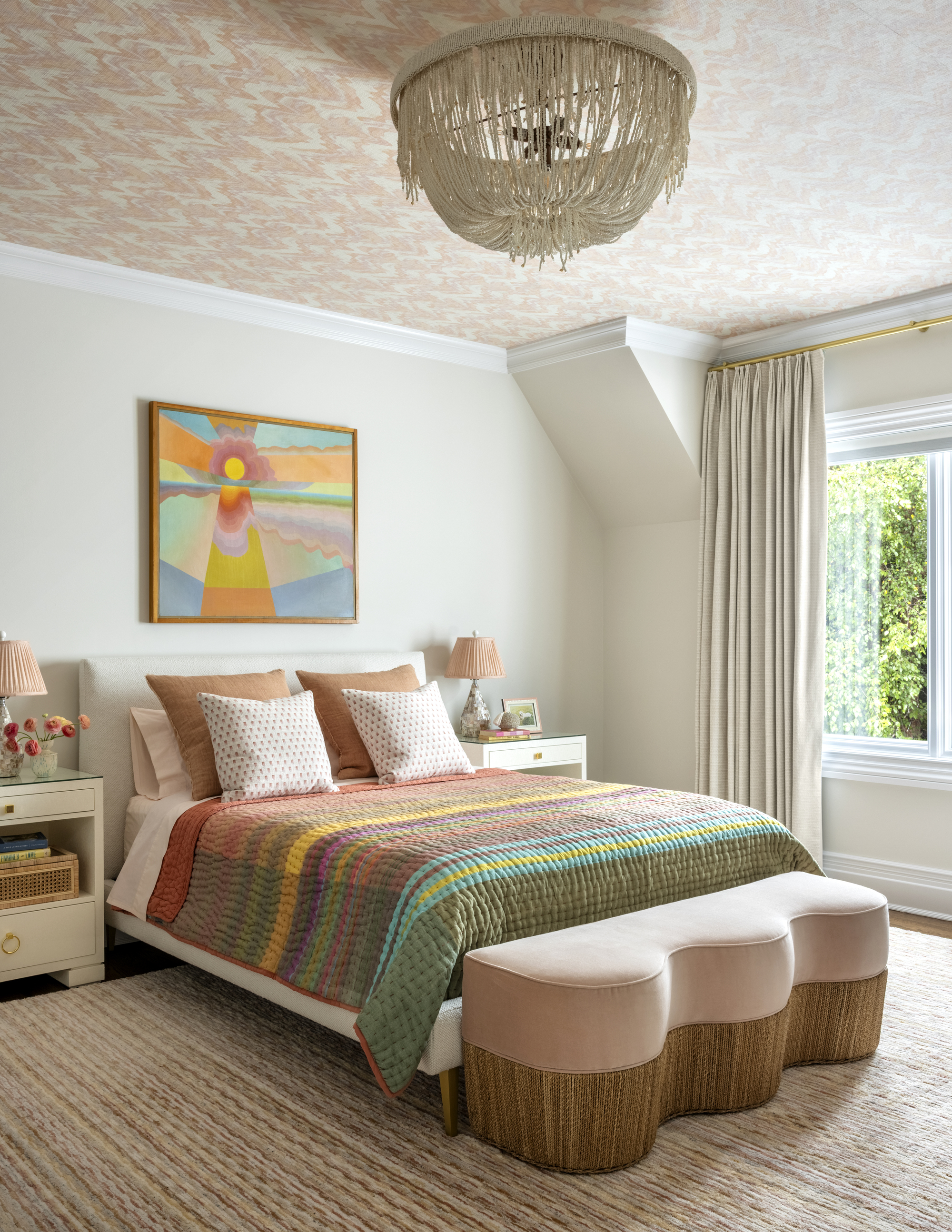 a colorful bed with pink sheets and vintage quilt, textural rug, storage unit and white bedside table