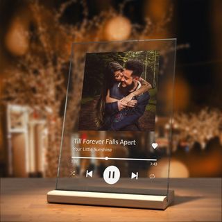 A customized music glass plaque sitting on a wooden table with a Christmas tree blurred out in the background