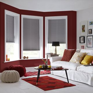 A red and white living room with grey roller blinds and white sofa