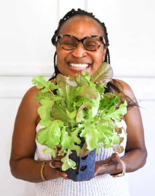 A smiling woman holds a mason jar of growing lettuce