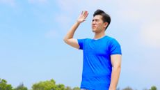 A man stands in the sun, squinting and blocking the sun with his hands