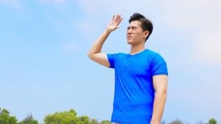 A man stands in the sun, squinting and blocking the sun with his hands