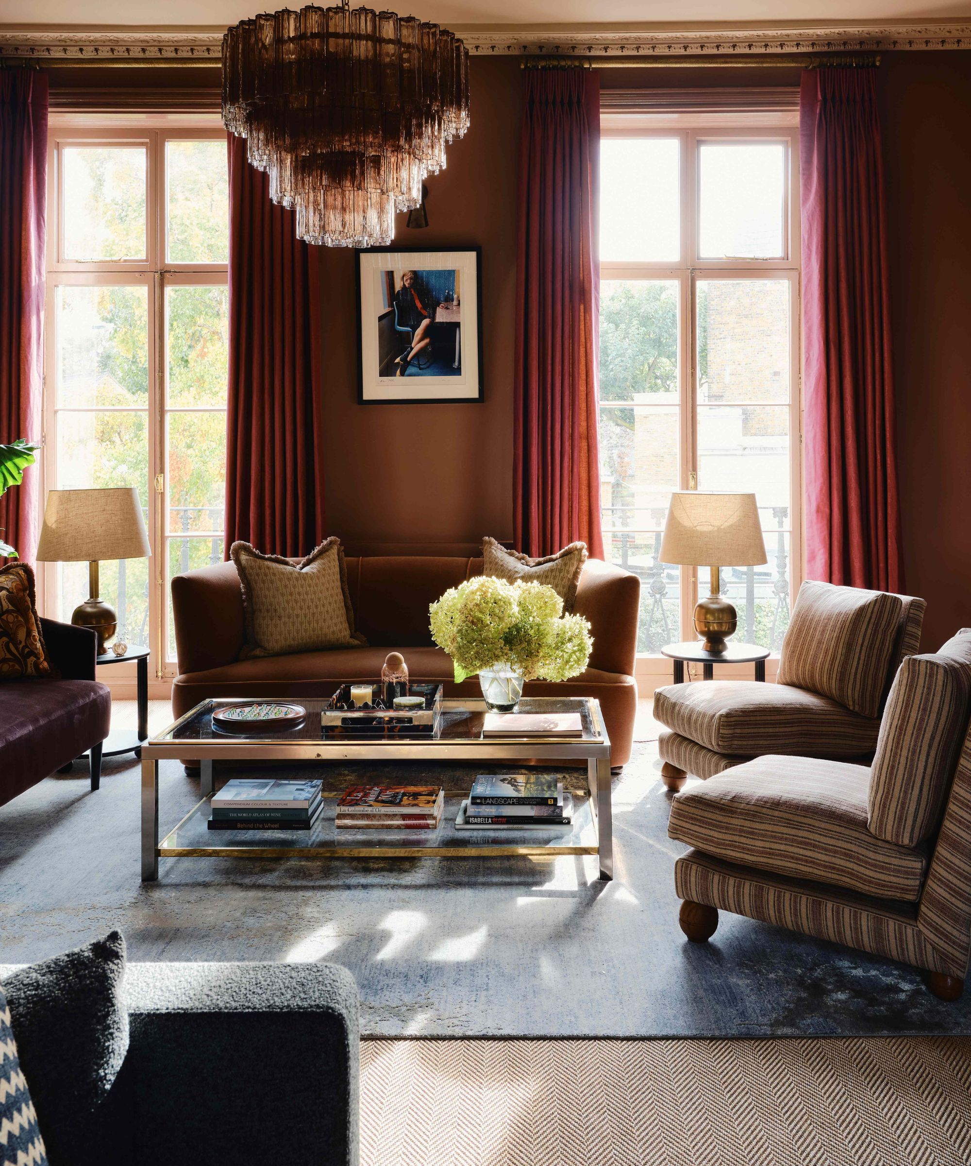 dark red living room with large windows, big chandelier, with blue rug and striped armchairs