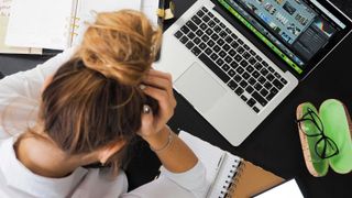 woman with head in hands next to laptop