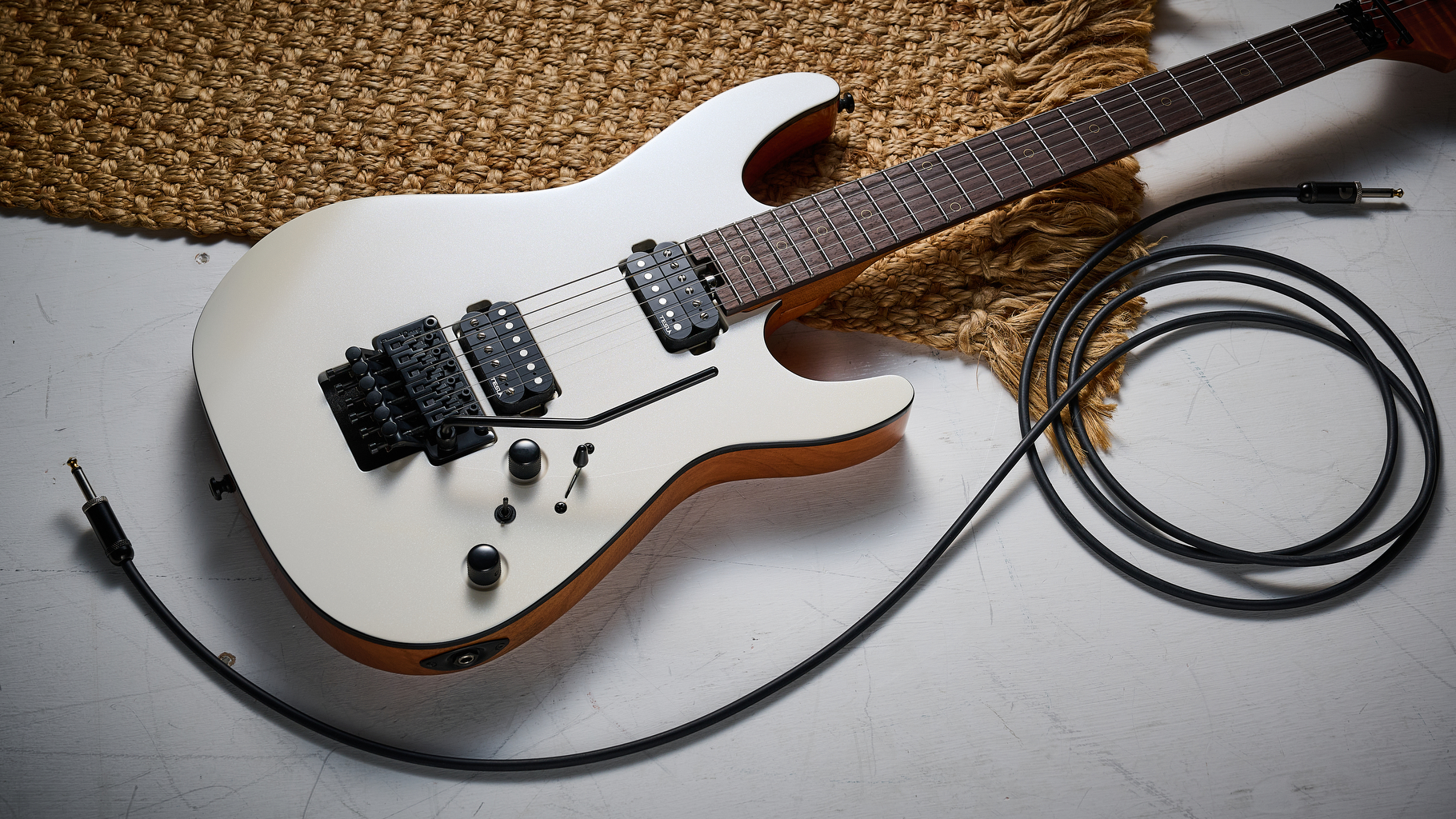 A Harley Benton Fusion IV HH electric guitar lies on a white floor with a rug and guitar cable nearby