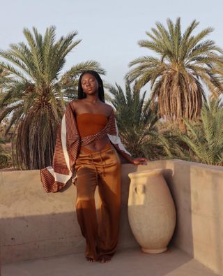 French girl's holiday wardrobe: @jullie.jeine wears rust satin trousers with an off-the-shoulder top