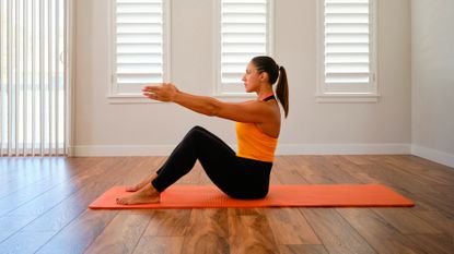 Woman sitting on exercise mat in fitness studio, reaching her arms out in front of her