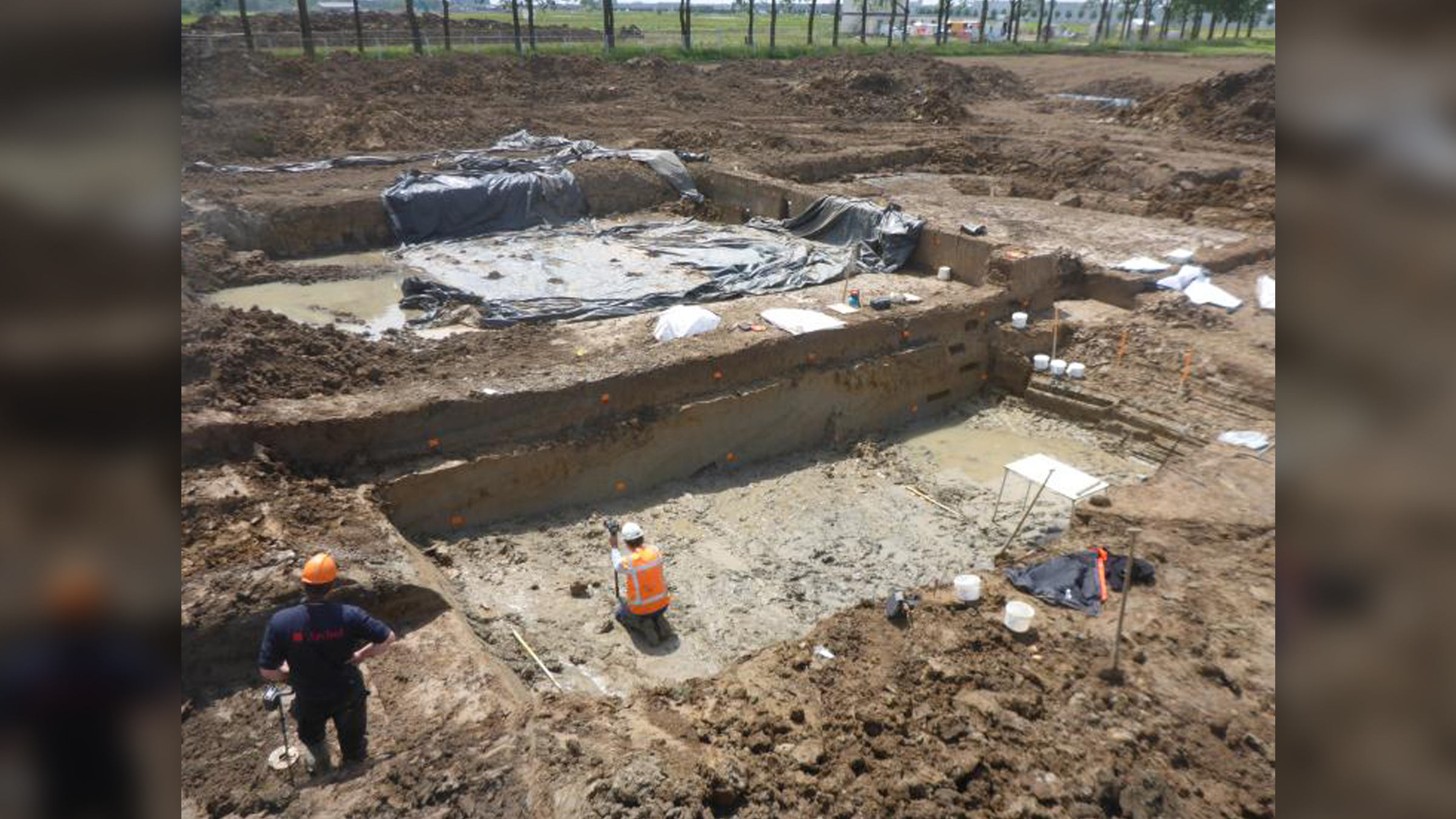 We zien twee archeologen een rechthoekig stuk in de grond graven.