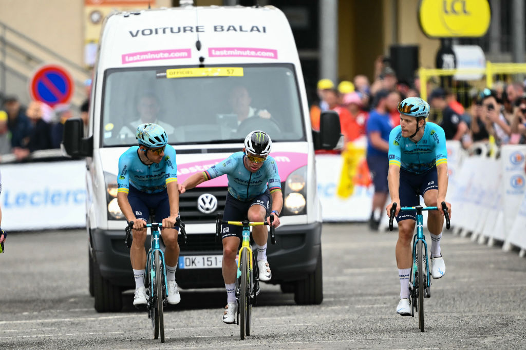 Astana Qazaqstan Team's British rider Mark Cavendish (C) cycles to the finish line flanked by teammates, ahead of the broom wagon vehicle, just within the cutoff time during the 14th stage of the 111th edition of the Tour de France