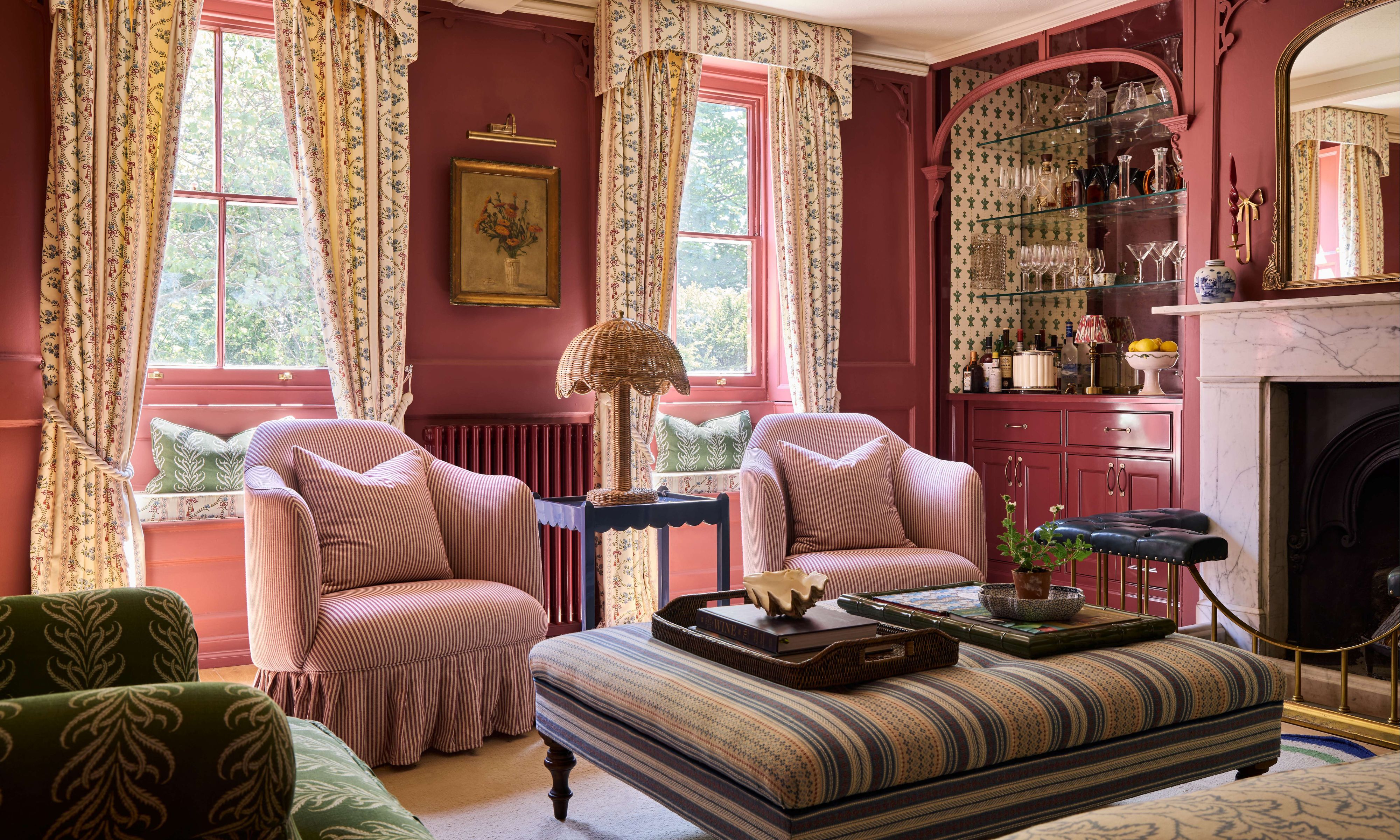 a red pink painted historic drawing room with window seats with patterned drapes and pelmet, skirted furniture and a marble fireplace