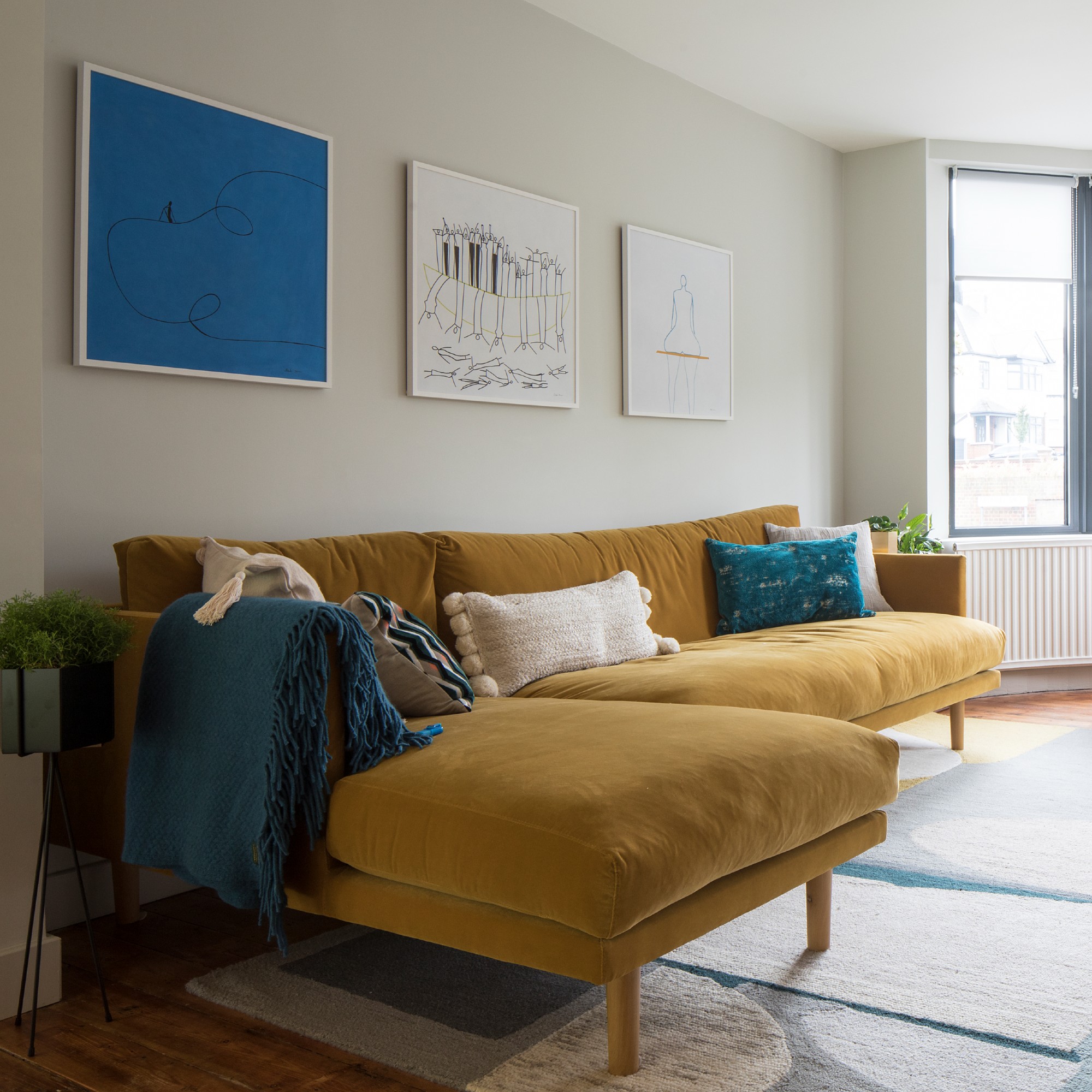 A living room with large windows painted in a neutral shade with a contrasting chaise sofa in mustard yellow velvet