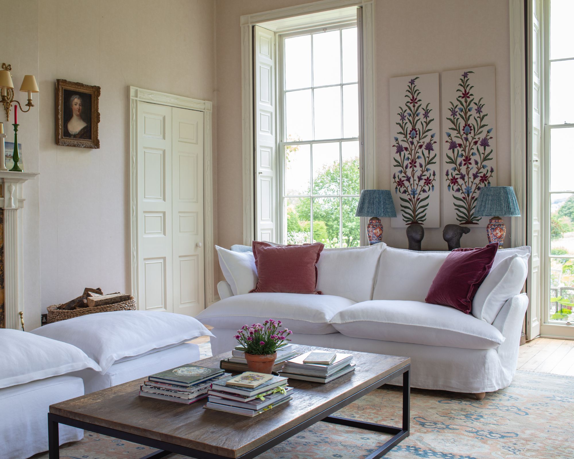 A crisp white sofa with two dark blush velvet cushions, with a coffee table in front, stacked with books.