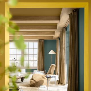 A spacious living room painted in a dark green shade with brown curtains and Dulux True Joy paint shade used on the door frame