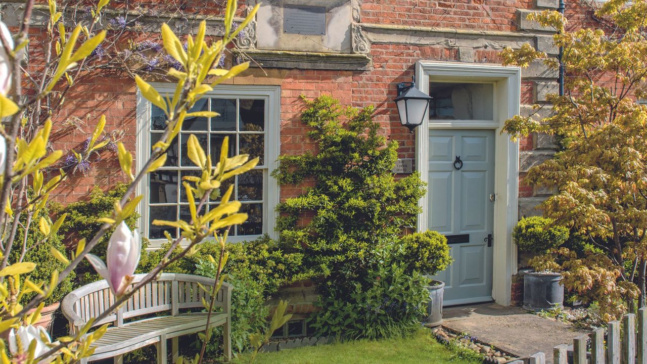 A red brick house with a a wooden front door and a magnolia tree outside it