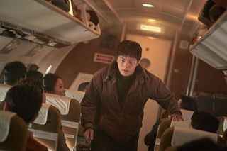 A man (Yeo Jin-goo) walks through a 1970s-era airplane, in 'Hijack 1971.'