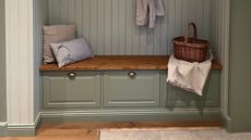 Built-in mudroom bench with sage green drawers, a warm wood top, decorative pillows, and a wicker basket against a matching beadboard wall