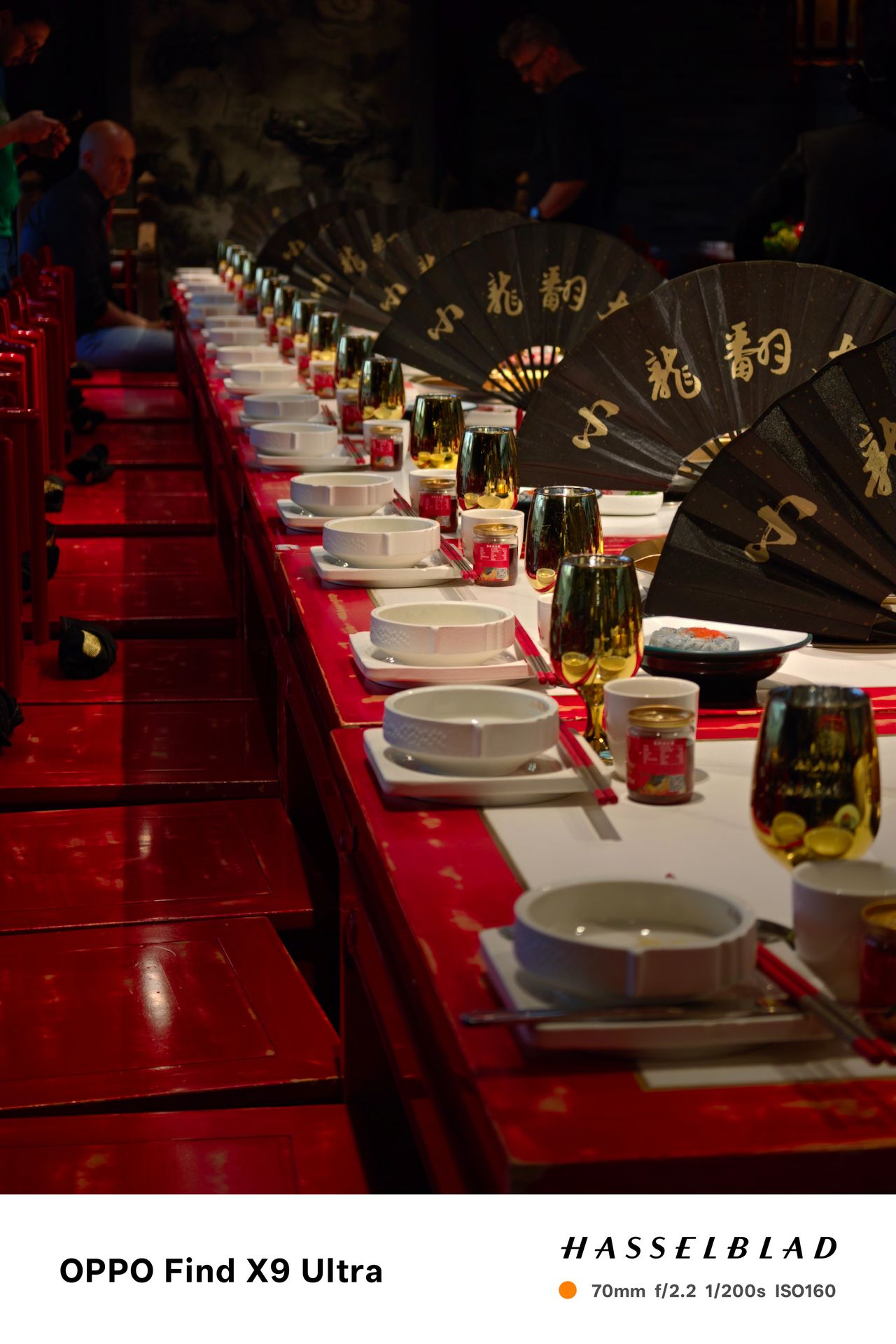 Long dining table set with bowls, glasses, and black folding fans in a dim restaurant