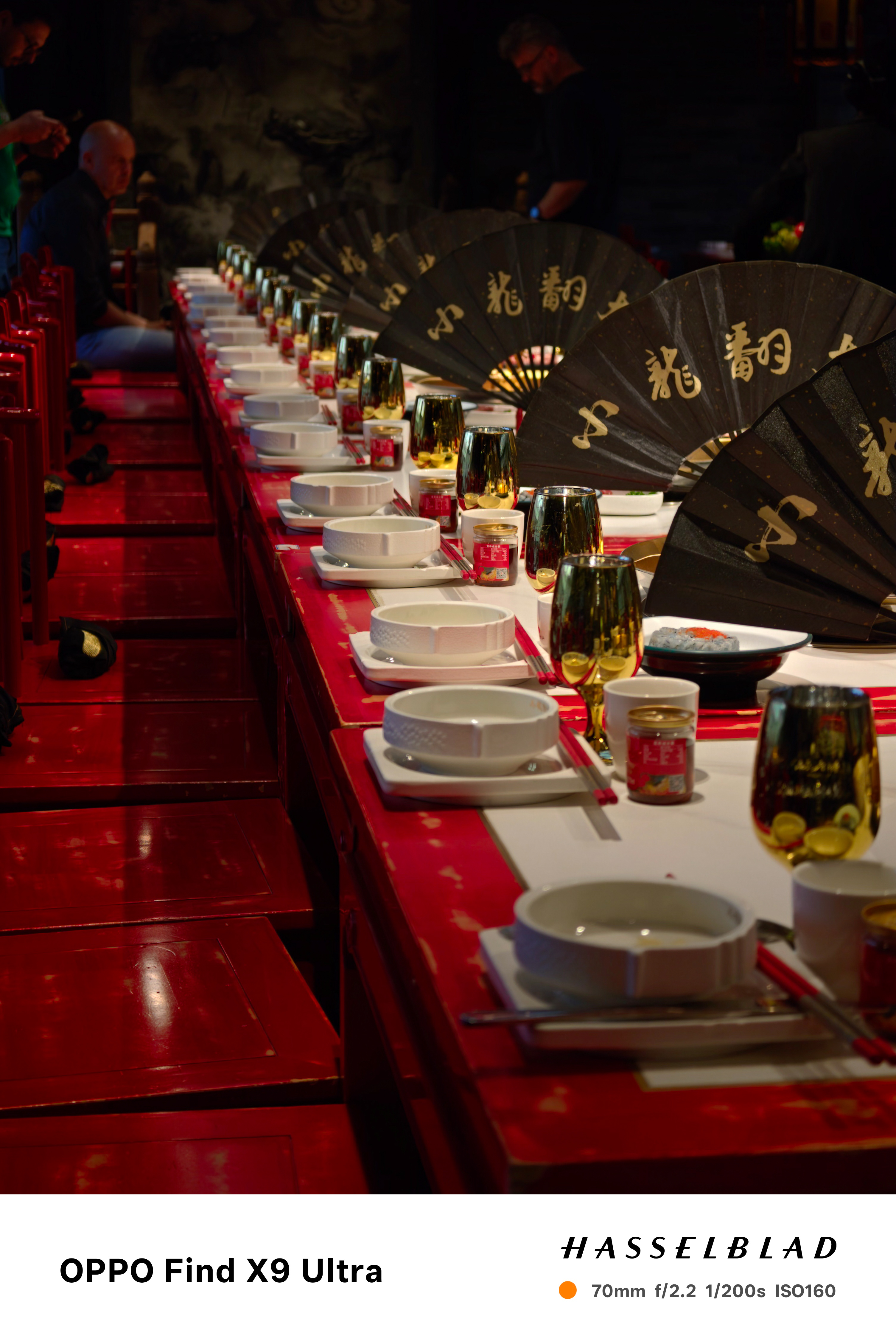 Long dining table set with bowls, glasses, and black folding fans in a dim restaurant