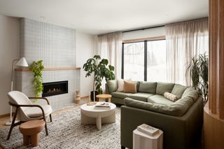 living room with light cream walls, lfireplace, large window, green sofa, white accent chair