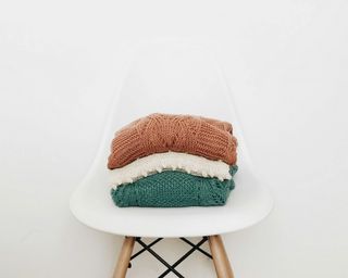 a stack of three sweaters folded up and sat on a white and wood stool