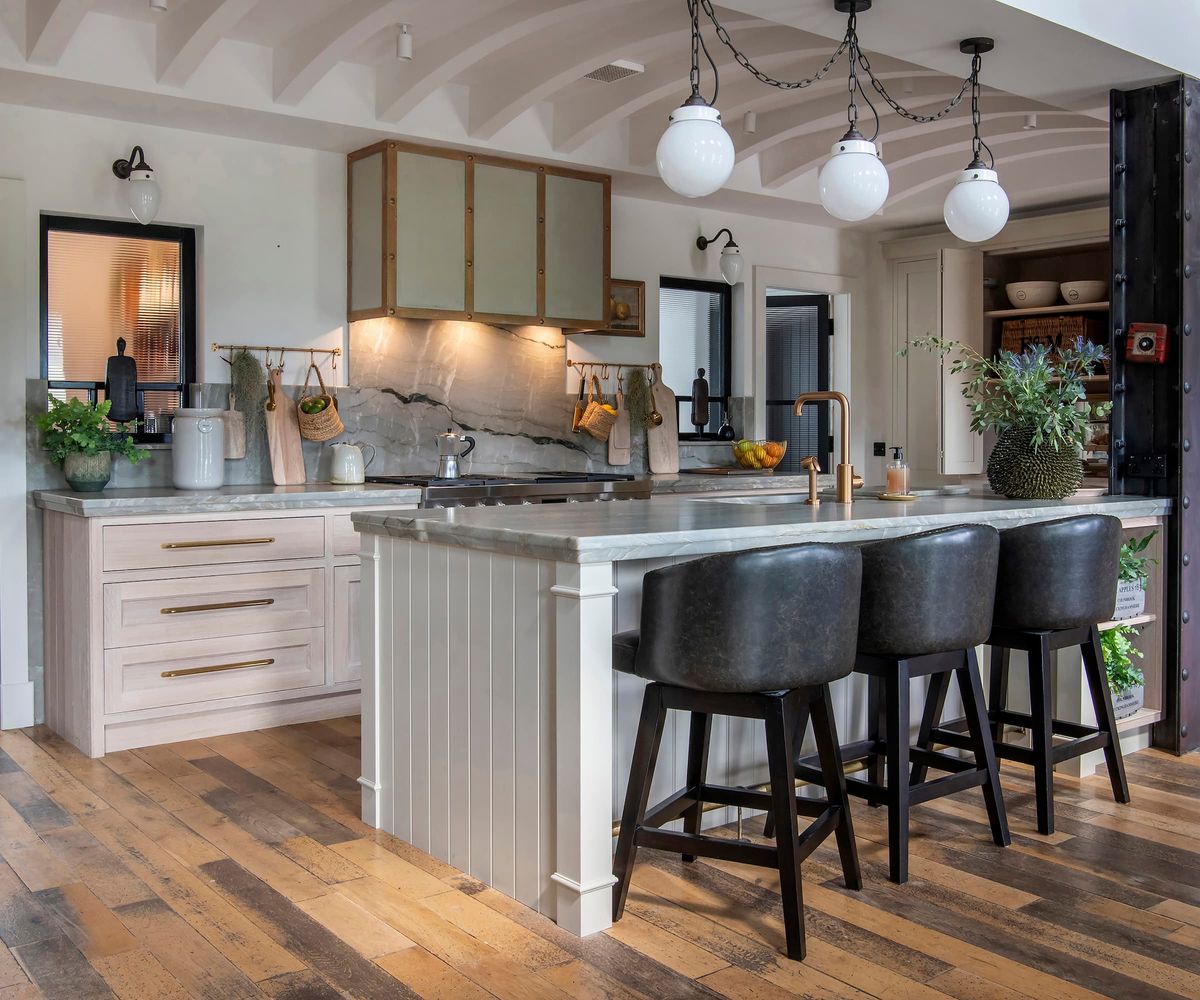 A kitchen with an island with a marble top and wooden panelled flooring and white cabinets