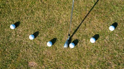 A golf club and six golf balls set up to demonstrate the natural arc of the club through the hitting zone