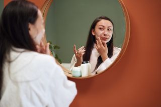 A women is looking in the mirror and applying moisturiser to her face