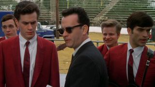 A concerned Tom Hanks stands in front of The Wonders while wearing sunglasses in That Thing You Do!