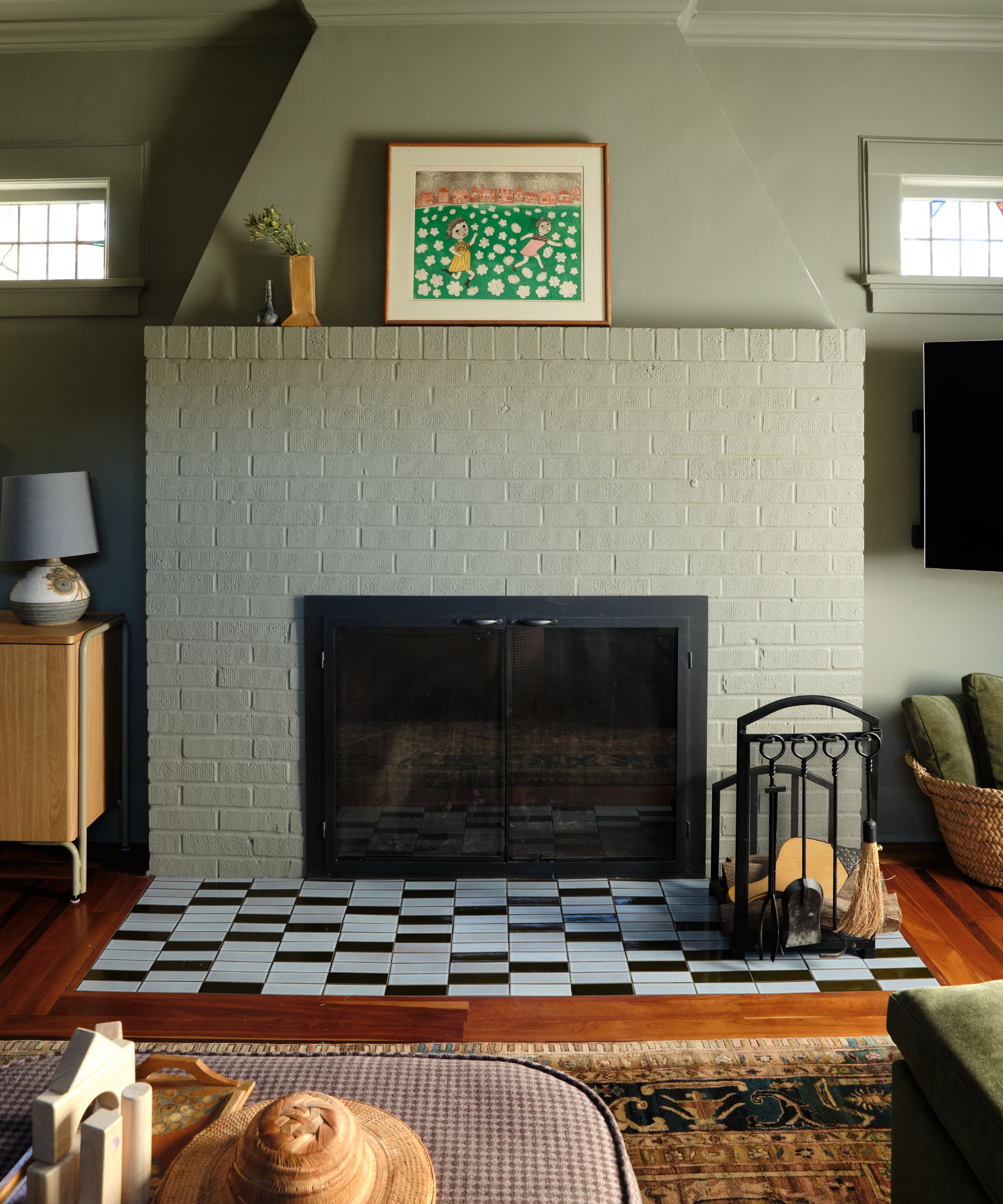 a moody green color drenched family room with a painted fireplace with checked tiles