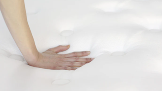 A hand feeling the surface of a white WinkBeds plus mattress